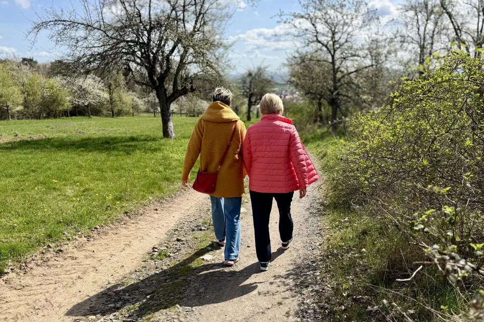 Anja Mattausch und eine Seniorin beim Spaziergang auf einem Feldweg im Frühling