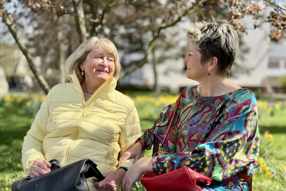 Anja Mattausch und eine Seniorin lachend auf einer Parkbank